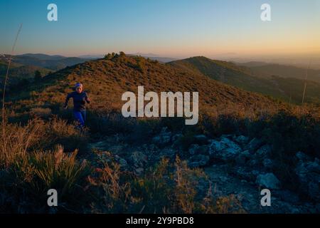 Sporty woman runs along a path in the mountains at sunrise. Stock Photo