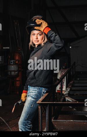 Woman in work gloves and welding helmet, holding a torch in a workshop Stock Photo