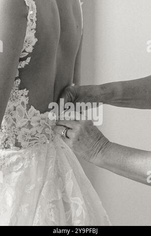 Black and white close-up of a bride’s lace dress being buttoned by mom Stock Photo