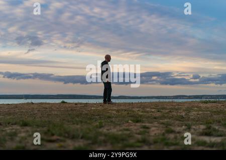 A man against the backdrop of the sunset sky on the shore of a lake. Stock Photo