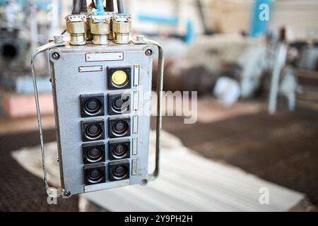 Overhead crane hand remote control panel in industrial petrochemical workshop out of focus hall with copyspace mockup. Movement faded old fashioned Stock Photo
