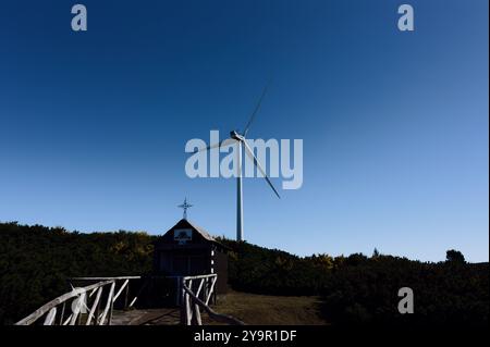 Wind turbine towering above rustic madeira chapel, tradition and innovation Stock Photo