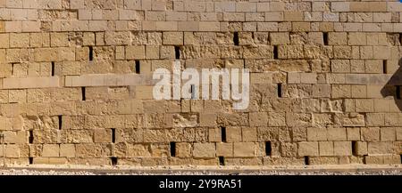 A landscape photograph capturing a detailed view of a wall made from large square limestone blocks in warm light yellow tones. The image highlights th Stock Photo
