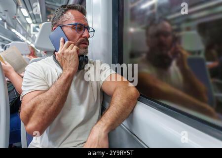 Middle-Aged Man in Casual Clothing Traveling on a Night Train While Talking on His Phone Stock Photo