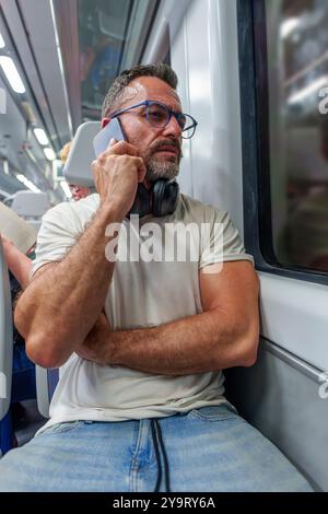 Middle-Aged Man in Casual Clothing Traveling on a Night Train While Talking on His Phone Stock Photo