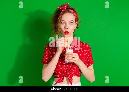 Photo portrait of pretty young girl hold milk glass drinking wear trendy red retro outfit isolated on green color background Stock Photo