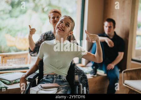 Smiling young woman in wheelchair giving thumbs up indoors Stock Photo