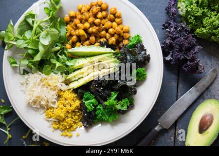 Healthy salad with quinoa, sauerkraut, spicy chickpeas, avocado and steamed kale. Flat lay image on light grey plate on dark blue background. Stock Photo