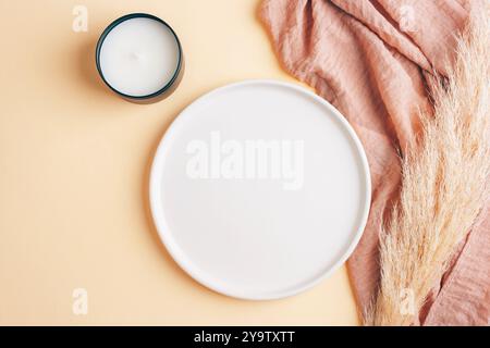 Empty plate, candle, pampas grass and cloth on table on neutral background. Top view, flat lay, mockup. Stock Photo