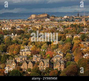 Blackford and the Grange areas of, Edinburgh, Scotland, UK. 11 October. Autumn colour is showing this year three weeks earlier than 2023, similar colours were photographed on November 5th last year. Temperature 11 degrees with a chilly SW wind at 26 km/h. Pictured: From Blackford Hill looking towards Edinburgh Castle under a broody sky and the Fife coast beyond, vibrant colour of the deciduous trees. Credit: Archwhite/alamy live news. Stock Photo