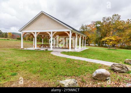 Tables under a wooden shelter in a lakeside park in the mountains on a cloudy autumn day. Autumn colours in background. Stock Photo