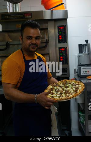 Kitchen assistant showing a pizza fresh out of the oven Stock Photo
