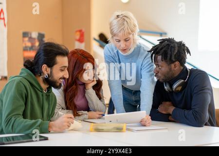 Group of diverse college students working together on academic project in university library. Multicultural team using laptop and notes for collaborat Stock Photo