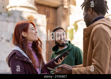 Happy diverse friends interacting outside. Multicultural group of young adults using smartphones and socializing in urban setting. Concept of friendsh Stock Photo