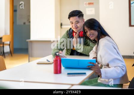 Asian college students working on academic assignment in university classroom. Diverse friends using smartphone and folder for collaborative study. Co Stock Photo