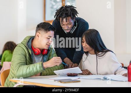Diverse group of college students working on digital tablet in university library. Multicultural friends collaborating on academic project. Concept of Stock Photo