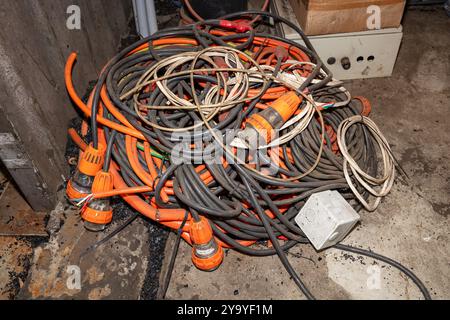 Photograph of old and dirty electrical power cables that have been left unattended and discarded on a dirty floor in a factory. Stock Photo