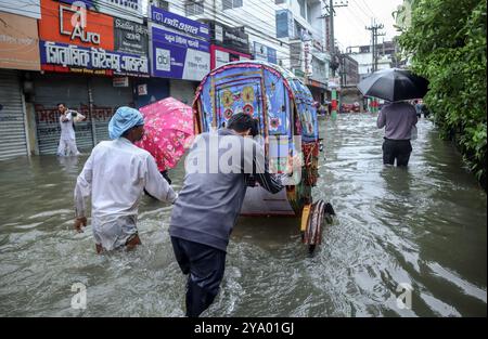 August 22, 2024, Feni, Chittagong, Bangladesh: Floods occur in Feni Sadar Upazila due to heavy rains. A boy pushes a rickshaw through floodwaters Stock Photo