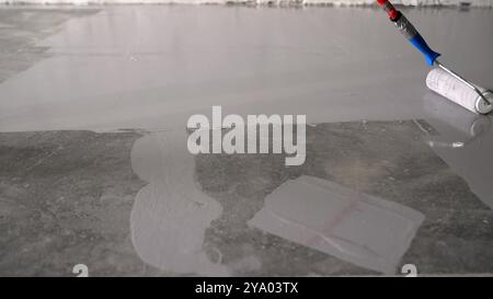 Construction worker is applying epoxy coating on a concrete floor using a roller. Stock Photo