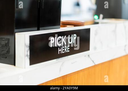 A close-up view of a counter with a sign that reads PICK UP HERE. The counter features a marble surface and wooden accents, creating a modern and invi Stock Photo