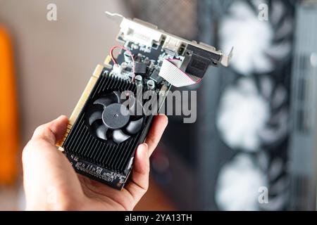 A person holding a graphics card with a black fan, showcasing its components. The background features a computer case with visible cooling fans, indic Stock Photo