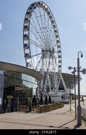 Large Ferris wheel next to a modern building in an urban space, Liverpool Stock Photo