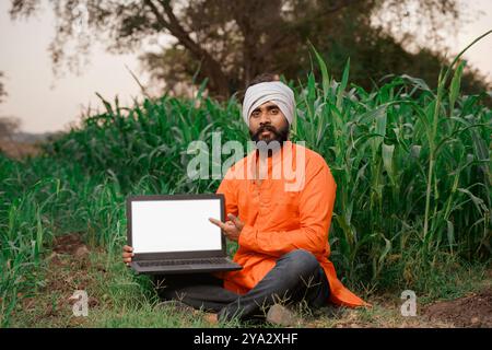 Indian rural farmer working on laptop in field of crops Stock Photo
