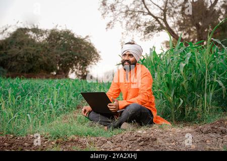 Indian rural farmer working on laptop in field of crops Stock Photo