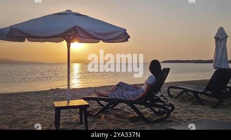 Carefree young woman lying on a sunbed at the beach watching the dawn taking a morning sunbathe with a view to the sea. Beautiful scene seaside, summe Stock Photo