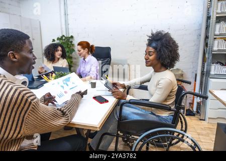 Side view of a cheerful african woman with disabilities sitting on wheelchair and male african colleague working in a coworking Stock Photo
