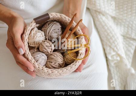 Female hands holding a crocheted basket with skeins of cotton yarn in natural tones Stock Photo