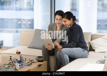 Two happy engaged diverse businesswomen using one tablet Stock Photo