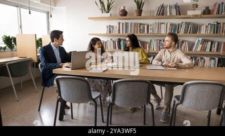 Diverse team of adult students talking at table in library Stock Photo