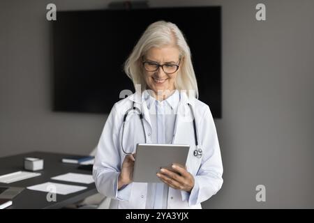 Smiling senior lady healthcare expert use pad in telemedicine Stock Photo