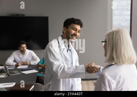 Grateful young man doctor shake hand to senior female teammate Stock Photo