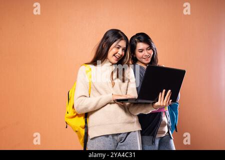 Students collaborate on a laptop, using colorful backpacks in a dynamic learning space Stock Photo