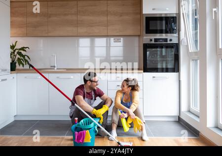 Young couple resting on floor and enjoying moments after cleaning their modern kitchen together during a bright afternoon at home Stock Photo