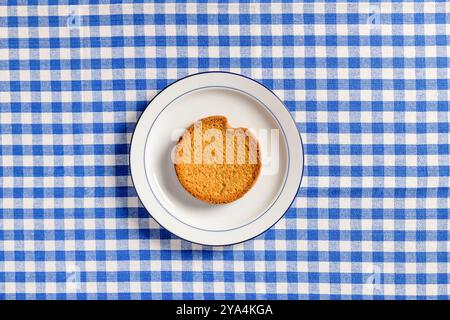 Top view of white ceramic breakfast plate with a typical dutch rusk and a  blue checkered tablecloth as background. Stock Photo