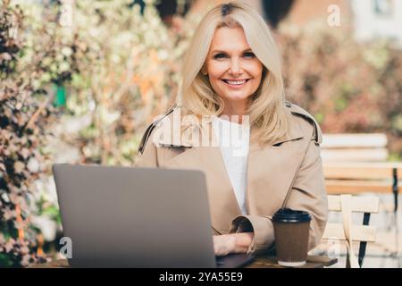 Photo of adorable gorgeous woman wear trench coat sitting on cafe terrace working remotely during vacation outdoors Stock Photo