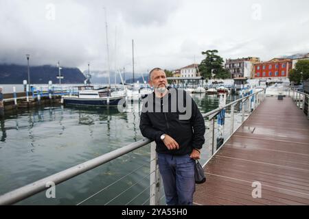 man stands on the lake embankment overlooking the boats on Lake Iseo Italy Stock Photo
