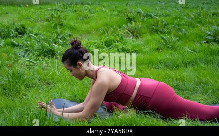 Young woman with brunette hair pulled back in a bun performs a yoga pose to work on hip opening dressed in a nice red yoga outfit of top and leggings Stock Photo