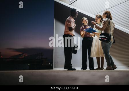 Young professionals having a discussion outdoors at dusk, exchanging ideas and engaging in a lively conversation, while expressing teamwork and Stock Photo