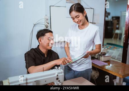 asian female employee showing the digital tablet to the male tailor Stock Photo