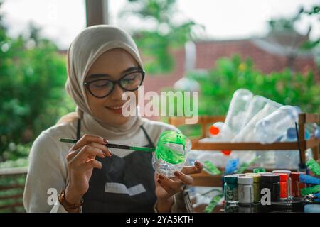 happy hijab woman brushing acrylic paint on plastic bottle Stock Photo