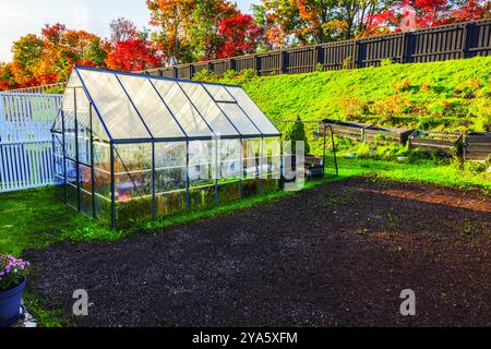 Greenhouse prepared for winter with stored items, set in an autumn garden with colorful trees and empty flowerbeds. Sweden. Stock Photo