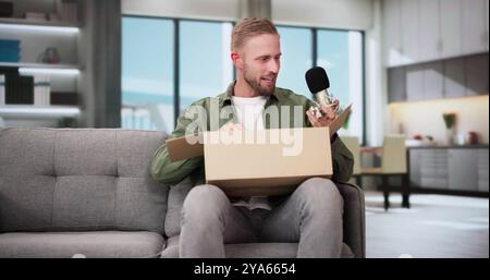 Smiling Young Man Sitting On Sofa Unpacking Received Parcel Stock Photo