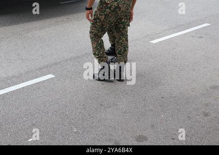 Close-up of camouflage military uniform and black boots on a textured asphalt road, depicting readiness and strength. Stock Photo