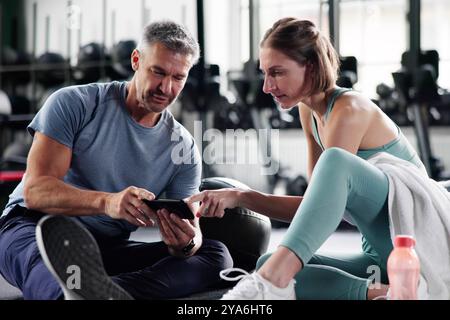 Fit Couple Talking And Looking At Phone At Gym After Workout Exercise Stock Photo