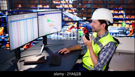 Warehouse Worker Manager Using Computer And Walkie-Talkie In A Warehouse Stock Photo