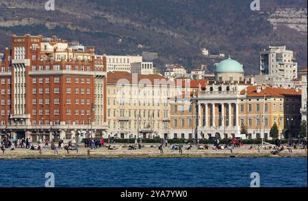 TRIESTE, Italy - March 9, 2014: Skyline of the Trieste seafront with its elegant historical buildings and people enjoying the sunny winter afternoon Stock Photo